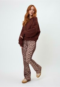 Felpa oversize marrone con maniche larghe abbinata a pantaloni a zampa d'elefante beige con stampa leopardata. Il modello si trova su uno sfondo chiaro indossando sneakers beige.