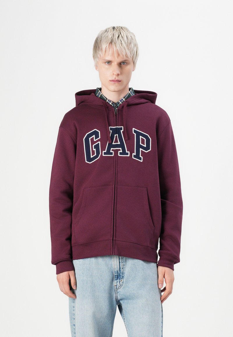 Bordeaux rode hoodie met grote "GAP" logo, voor zakken en een gevoerde capuchon. Gedragen over een geruit shirt, gecombineerd met lichte spijkerbroek.