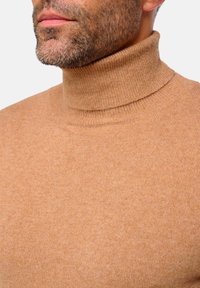 Hellbrauner Rollkragenpullover mit gerippter Textur. Merkmal ist der hohe Halsausschnitt und das taillierte Design, gefertigt aus weichem, warmem Material.