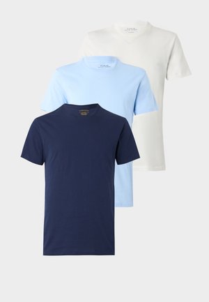 Trois t-shirts unis à col rond bleu marine, bleu clair et blanc, présentés en couches sur un fond neutre.