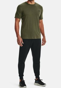 Olivengrøn kortærmet T-shirt med rund halsudskæring, kombineret med sorte joggers. Har et lille sort logo på brystet og et tætsiddende design.