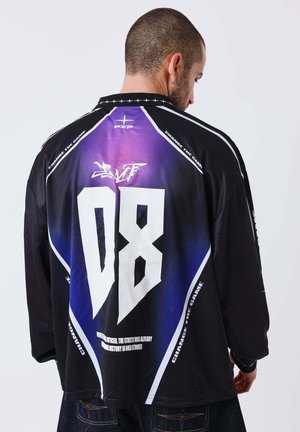 Mann mit rasiertem Kopf, der ein schwarz-lila Sporttrikot mit großer weißer "08" und dem Text "Change the Game" auf dem Rücken trägt.