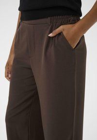 Bruine elastische broek met tailleband en zijzakken, met een smooth textuur en een getailleerde pasvorm. Zichtbare stiksels langs de zakken en naden.