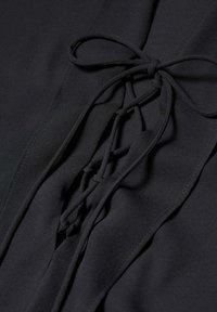 Tissu noir présentant un détail de nœud noué avec des accents tissés, une texture lisse et un éclat subtil, mettant en valeur un design élégant.
