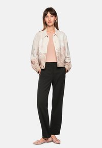 Hellfarbene Bomberjacke mit floralem Muster, kombiniert mit einem rosa Oberteil und schwarzen, maßgeschneiderten Hosen. Weicher Stoff und flache rosa Schuhe.