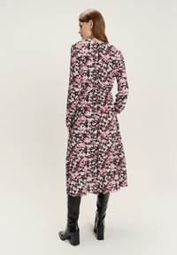 Bloemenprint jurk met lange mouwen, een cinched taille en een vloeiende silhouet. De stof is lichtgewicht in tinten roze en zwart.