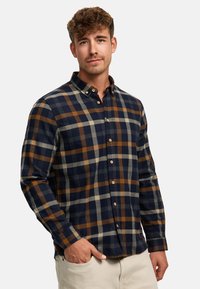 Flanellskjorte med knapper i marineblå, brun og kremrute; langermet; myk tekstur; krage med knappestolpe foran.