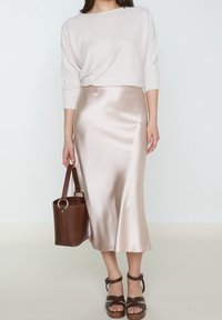 Ljust rosa stickad tröja, satäng midi kjol i mjuk beige, brun läderhinkväska och sandaler med remmar och klack i brunt.