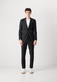 Črn kostim z blazerjem na eno gumbe in ujemajočimi hlačami. Obut čez belo majico, dopolnjen z belimi supergami in gumijastimi podplati.