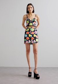 Čierny crop top s kvetinovým vzorom a zodpovedajúca sukňa s farebnými kvetmi a srdcami. Ozdobené zúbkovanými okrajmi, doplnené čiernymi platformami.