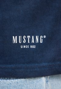 T-shirt en coton marine avec le logo blanc "MUSTANG" et le texte "SINCE 1932" imprimé sur le devant, présentant une texture lisse et un design simple.