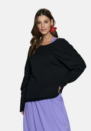 Czarny, oversize sweter z szerokim dekoltem i opadającymi ramionami. Miękka tekstura, w połączeniu z jasnofioletową spódnicą.