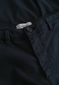 Sötétkék pamut nadrág, gombos záródással és övbújtatókkal. A címke felirata: "GABBA." Az anyag textúrája puha és minimális fényű.