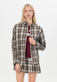 Brown and white plaid button-up shirt worn over a maroon top, paired with a matching plaid skirt. Cotton fabric with a relaxed fit.