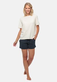 Hellbeige Baumwoll-T-Shirt kombiniert mit marineblauen Shorts mit weißen Punkten. Die Shorts haben einen elastischen Bund und Taschen.