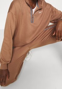 Brun fleece med kvartslång dragkedja och en texturerad svart och vit krage, ihop med matchande bruna byxor med sidostripdetalj.