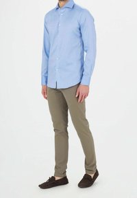 Camicia azzurra chiara a maniche lunghe con colletto a punta, chiusura con bottoni, abbinata a pantaloni verde oliva con trama e mocassini marrone scuro.