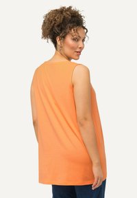 Ärmelloses oranges Baumwolloberteil mit rundem Ausschnitt, lockerer Passform und gewelltem Saum; glatte Textur und schlichtes Design.