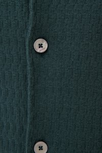 Dunkelgrüner Strickstoff mit einem strukturierten Muster und zwei runden, vierlochigen Knöpfen in einer vertikalen Reihe.