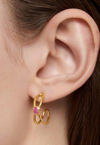 Orecchino a cerchio in oro con un design intrecciato, caratterizzato da un accento in pietra preziosa rosa. Indossato all'orecchio, mette in mostra finiture lisce e forme organiche.