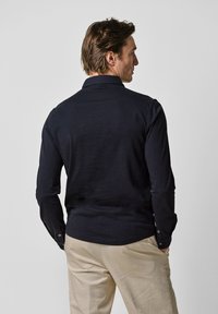 Mörkblå långärmad skjorta med krage, knäppta manschetter och en slät yta, kombinerad med ljusbeige byxor.