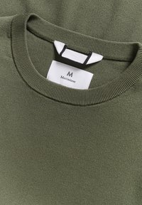 Olivově zelený pletený svetr s kulatým výstřihem. Štítek viditelný uvnitř výstřihu, se černobílými akcenty. Hladká textura.