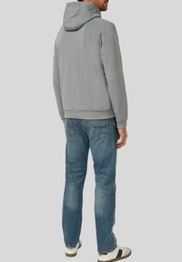 Grauer Kapuzenpullover mit Kordelzug, geripptem Saum und Bündchen, kombiniert mit legeren blauen Jeans und weißen Sneakers mit schwarzen Akzenten.