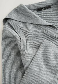 Pelēks ribots džempers ar platām apkaklēm un salocītām detaļām. Auduma tekstūra ir maiga, un tai ir vienmērīgs vertikāls ribu raksts. Zīmola etiķete redzama.