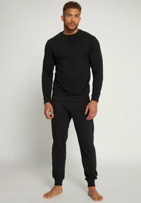 Chemise noire à manches longues avec des pois blancs et des poignets côtelés, assortie à un pantalon de jogging noir. Le tissu semble doux et confortable.