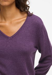 Maglione viola a V in morbido tessuto con maniche lunghe, caratterizzato da una texture liscia e dettagli di cucitura sottili lungo il collo.