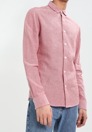 Pitkähihainen paita vaaleanpunaisesta kankaasta, jossa on hillitty tekstuuri, napillinen etuosa, kaulus ja rento istuvuus.