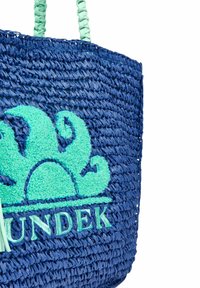 Sac en paille tressée bleue avec un logo vert et un motif décoratif en vagues. Dispose de poignées torsadées de couleur menthe et d'un corps texturé et flexible.
