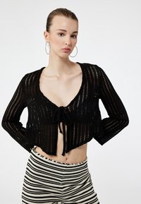 Czarny, krótki sweter z dzianiny z zapięciem na sznurek i otwartym splotem. Połączony z wysokim stanem w paski. Prosty design.