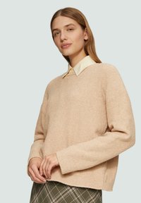 Helles rosa, strukturiertes Sweatshirt aus weichem Material. Verfügt über einen runden Halsausschnitt und lange Ärmel, die über ein Hemd mit Kragen getragen werden.