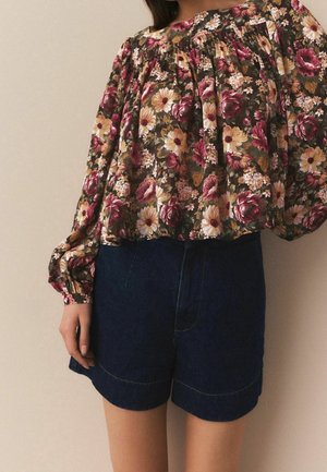 Kwietna bluzka z bufkami na rękawach na ciemnym tle; zawiera odcienie różu, żółci i bieli kwiatów. Ciemne szorty z denimu z widocznymi przeszyciami.