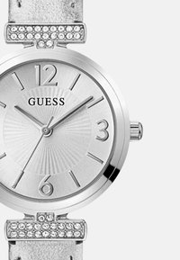 Hõbedase tooni kell, millel on tekstuuriga tahvel, araabia numbrid 12 ja 3 juures ning rhinestone'idega kaunistatud rihm. Omab poleeritud metallkorpust.