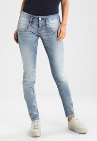 Jeans skinny azzurri chiari con un lavaggio sbiadito, design a cinque tasche e dettagli di cucitura sottili. Abbinati a sneaker bianche.