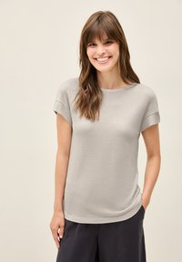 Grijs T-shirt met korte mouwen, gemaakt van een zachte gebreide stof; heeft een ronde hals en een comfortabele pasvorm met een subtiele glans. Draagt met donkere broek.