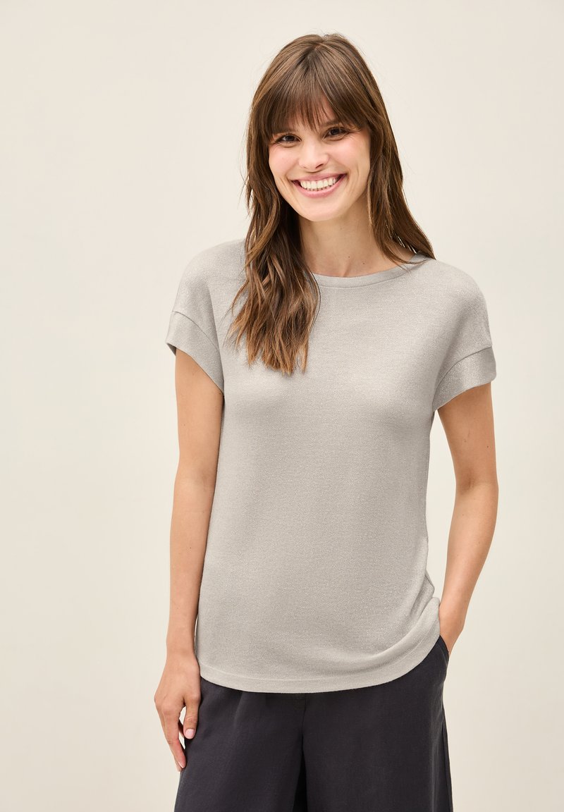 Grijs T-shirt met korte mouwen, gemaakt van een zachte gebreide stof; heeft een ronde hals en een comfortabele pasvorm met een subtiele glans. Draagt met donkere broek.