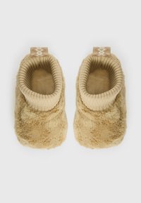 Tan fleece tøfler med ribbestrikket mansjett, som har en myk tekstur og en dekorativ løkke på baksiden for enkel påføring.