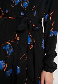 Robe noire avec un motif floral bleu et des accents orange, comprenant une ceinture, des boutons et des manches longues. Fabriquée à partir d'un tissu texturé.