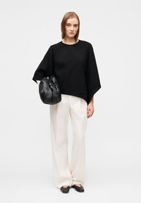 Črn prevelik pulover z širokimi rokavi, kombiniran z belimi širokimi hlačami. Model drži črno usnjeno torbico z zategnjenim zgornjim delom.