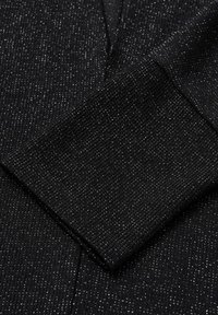 Zwarte ribstof met metallic draadaccenten. Close-up van de mouw en textuur met verticale lijnen en een subtiele glans.