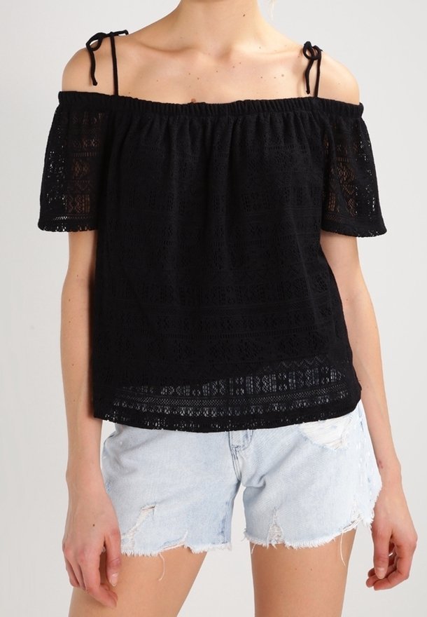 Haut noir épaules dénudées avec détails en dentelle, encolure élastique et manches courtes. Associé à un short en jean clair avec ourlet effiloché.
