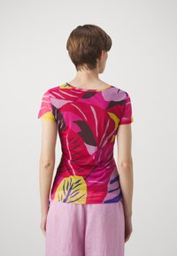 Lyhythihainen, sopivasti istuva t-paita kirkkaan vaaleanpunaisena, jossa on suuri trooppisen lehden painatus keltaisena, purppurana ja tummanruskeana. Sujuva, kevyt kangas.