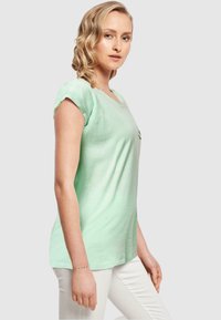 Mintgrünes T-Shirt mit Rundhalsausschnitt und umgeschlagenen kurzen Ärmeln. Aus leichtem Stoff gefertigt, mit einem dezenten Design auf der Vorderseite.