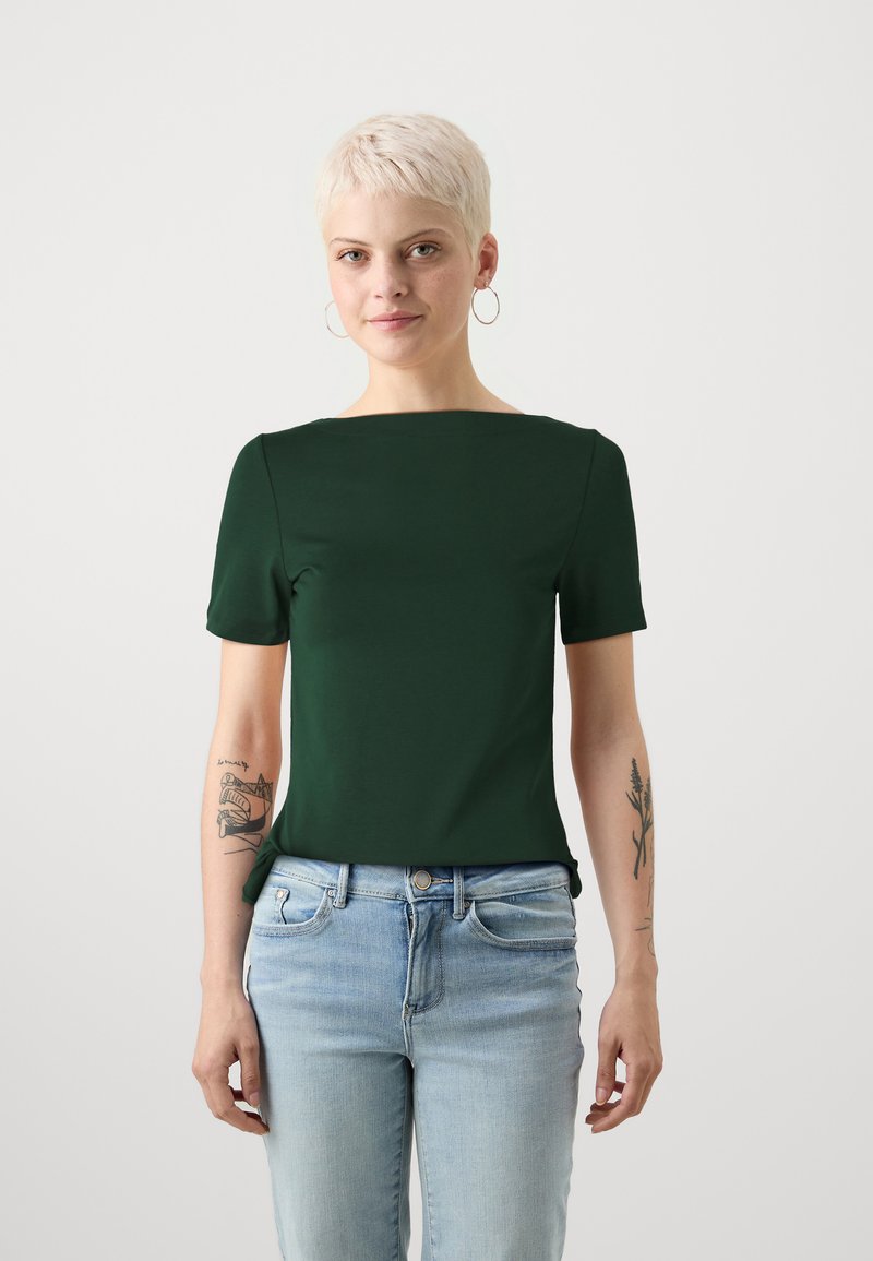 Mørkegrønn t-skjorte med korte ermer og firkantet hals, laget av glatt stoff. Båret med lyseblå jeans, som viser en uformell stil.
