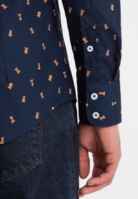 Marineblauwe shirt met een oranje schaakstukpatroon, lange mouwen, knoopmanchetten en een ronde zoom. Gemaakt van geweven stof met een gladde textuur.