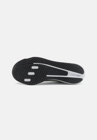 Semelle de chaussure de sport noir et blanc avec un motif de grip texturé et trois sections de cushioning blanches rectangulaires.