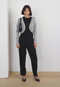 Gray cropped cardigan over a black top, paired with black loose-fitting trousers and black pointed-toe heels. Minimalistic design, smooth texture.